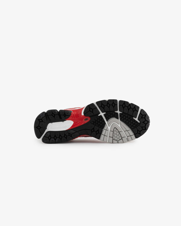 The image shows the outsole of a red and black running shoe, featuring a textured rubber surface with grooves and patterns for traction. The New Balance branding is subtly visible on the shoes side, highlighting its athletic design.