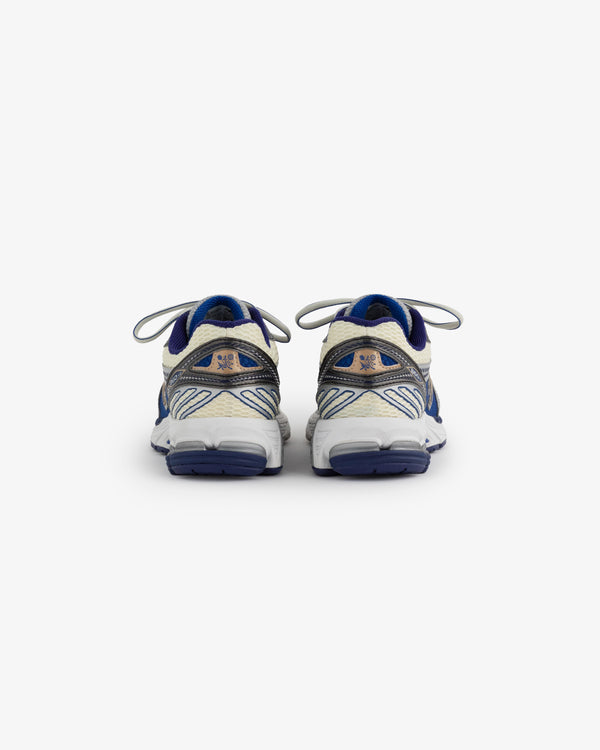 A pair of New Balance 860v2 sneakers is displayed from the back, showcasing the blue and beige colorway. The shoes feature a sleek design with prominent branding and reflective accents, perfect for athletic wear.