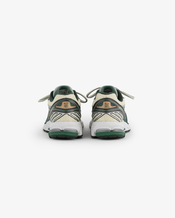 A pair of New Balance 860v2 sneakers is displayed from the back, showcasing a cream and green color scheme. The shoes feature a textured design with laces and a cushioned sole, highlighting their sporty and stylish appearance.