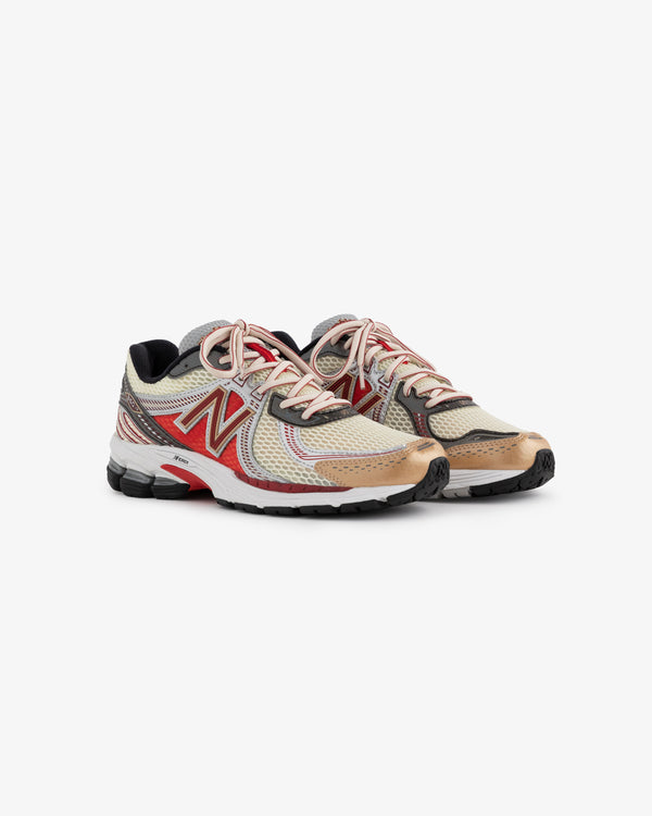 A pair of New Balance 860v2 running shoes in a light beige and red color scheme. The shoes feature a mesh upper with reflective accents and a cushioned sole, designed for comfort and support during athletic activities.