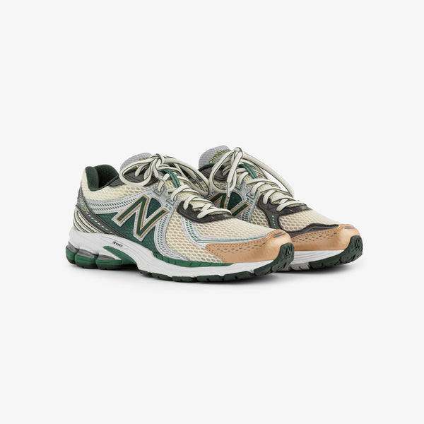A pair of New Balance 860v2 running shoes in a light beige and green color scheme. The sneakers feature a mesh upper, cushioned sole, and prominent logo on the side, designed for comfort and performance.
