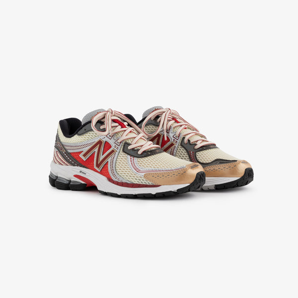 A pair of New Balance 860v2 running shoes featuring a beige and red mesh upper with black accents. The shoes are displayed side by side, showcasing their sleek design and cushioning sole.